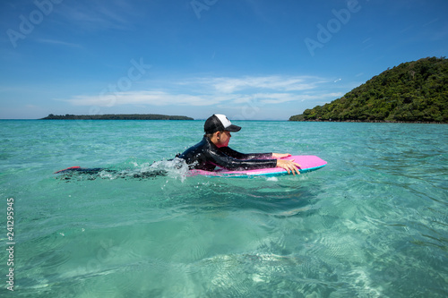 Asian kid surfing at turquoise sea on sunshine day with blue sky background