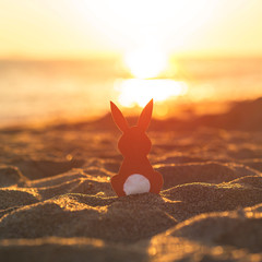 Creative easter concept photo of red paper bunny on the sand on the beach at sunset. Concept. Easter celebrations in tropical countries.