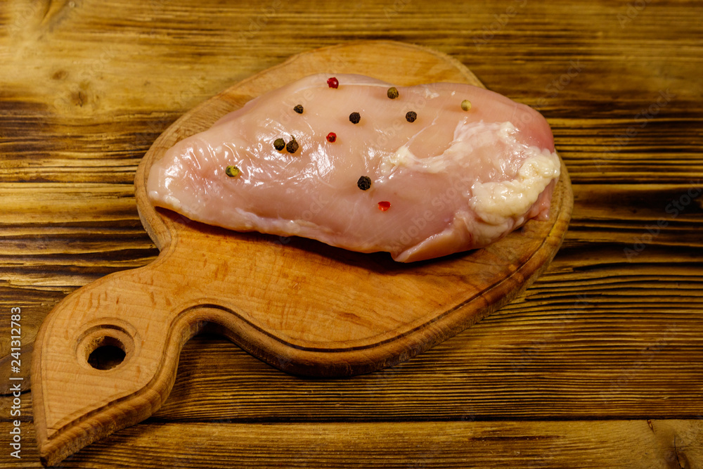 Raw chicken breast on cutting board on wooden table