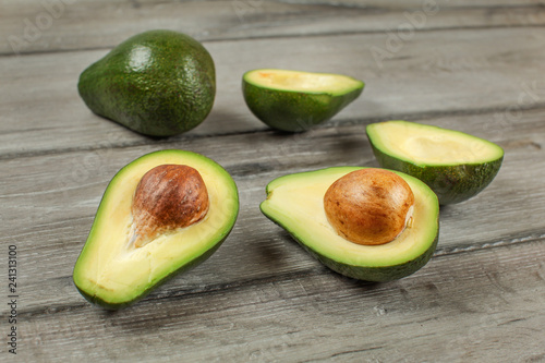Avocados cut in half seed visible, one whole green pear in background, on gray wood desk