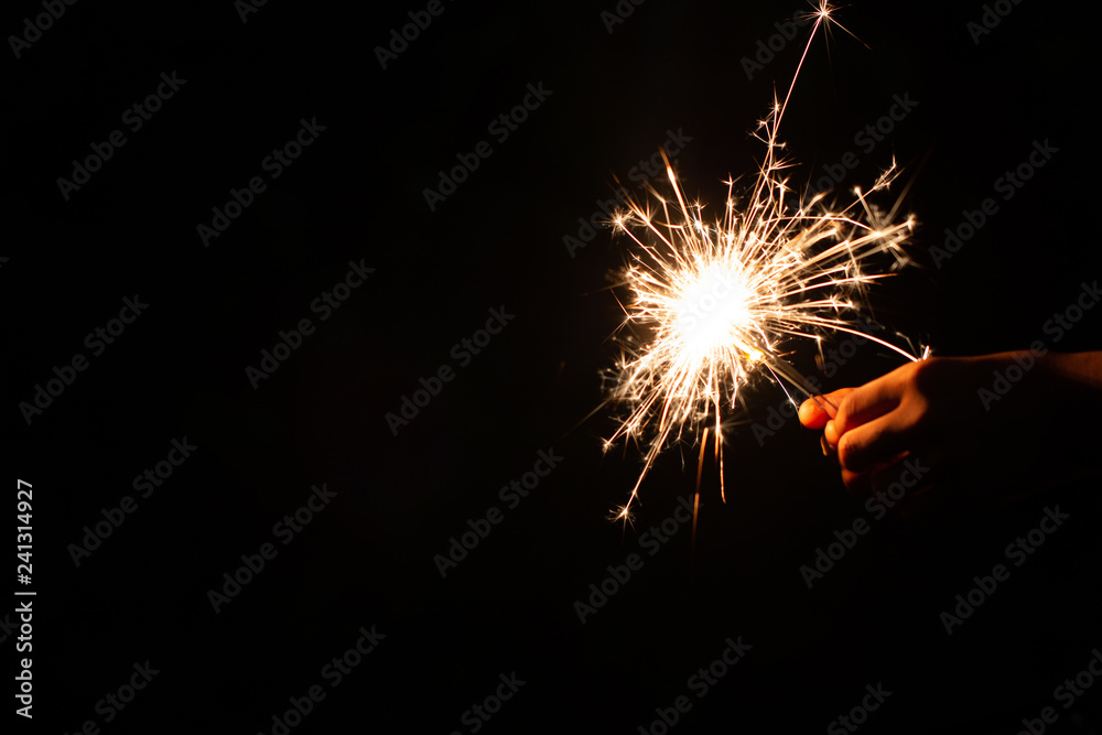 New year party burning sparkler with kids hand on black background. Children hold glowing holiday sparkling hand fireworks