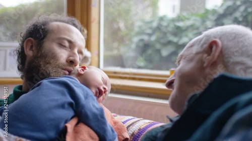 New father kisses his newborn baby as grandfather looks on photo