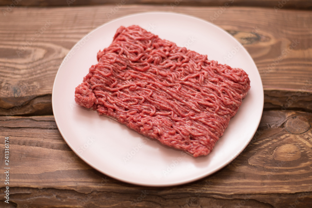 Fresh minced meat on a plate on a wooden background for cooking. Fresh minced meat on a plate on a wooden background for cooking.