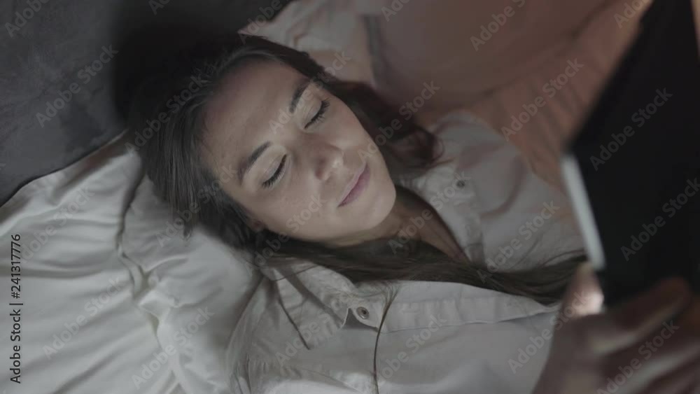 Sleepy young woman using tablet pc in bed. High angle view of beautiful young woman yawning and using digital tablet in bedroom at night. Networking concept Sleepy young woman using tablet pc in bed. High angle view of beautiful young woman yawning and using digital tablet in bedroom at night. Networking concept