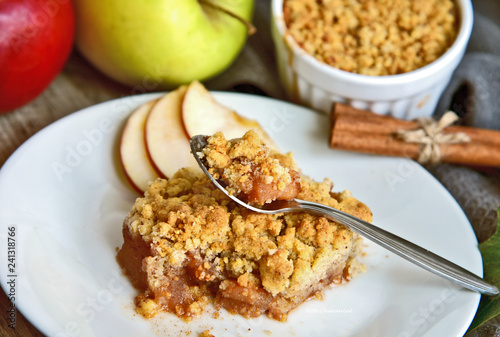 Apple crumble on with dish with spoon and fresh green and red apple with cinnamon stick on wooden floor. Easy and Basic dessert menu.