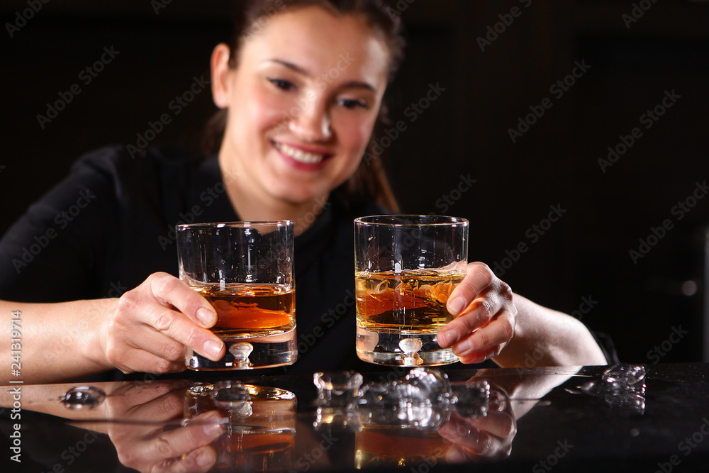 The bartender girl smiles and pours whiskey into glasses and adds ice. Photo on the bar in the restaurant. Girl out of focus.