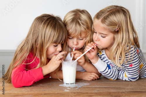 Three girls blowing bubbles in a glass of milk with drinking straws