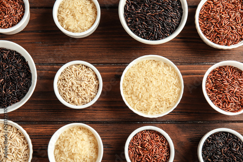 Bowls with different types of rice on wooden background  top view