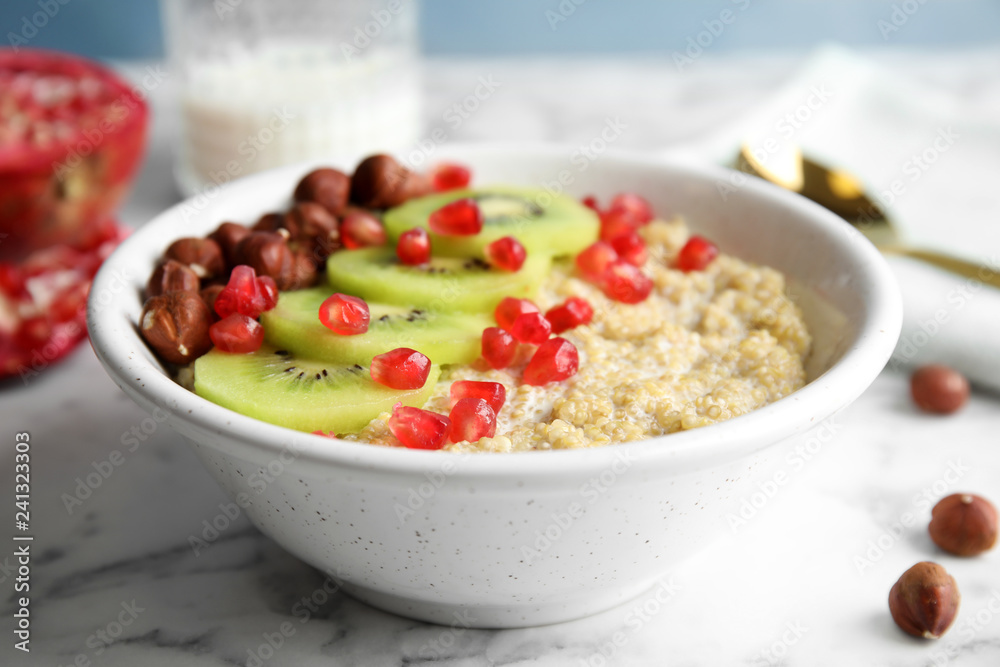 Bowl of quinoa porridge with hazelnuts, kiwi and pomegranate seeds on marble table Bowl of quinoa porridge with hazelnuts, kiwi and pomegranate seeds on marble table