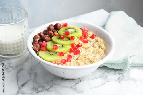 Bowl of quinoa porridge with hazelnuts, kiwi and pomegranate seeds on marble table