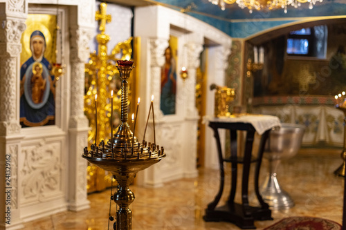 Many burning wax candles in the orthodox church or temple on golden warm background