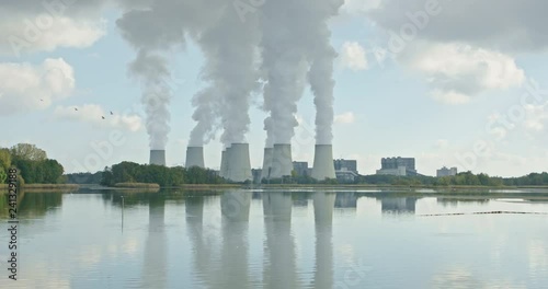 Lignite power plant in front of a lake, birds fly past, the smoke rises steadily in the reflected, an idylic picture of industry and nature photo