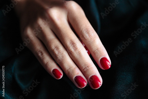 Gorgeous manicure, clssic red color nail polish, closeup photo. Female hands over dark fur background