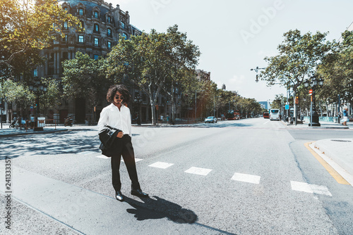 Wide-angle view of a young curly Asian guy in a white shirt and with the blazer in his hand during passing the crosswalk  a handsome businessman in sunglasses on the pedestrian crossing © skyNext