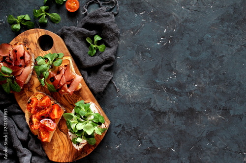 Variety of small sandwiches with prosciutto, tomato, light cheese, fresh salad and balsamic vream on dark background. Top view with copy space. photo