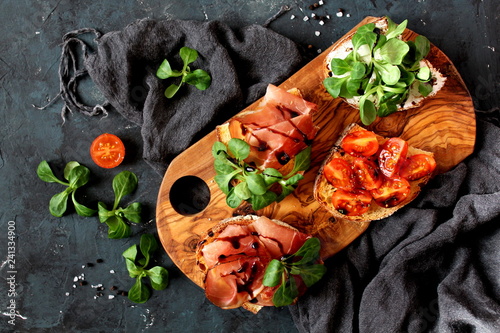 Variety of small sandwiches with prosciutto, tomato, light cheese, fresh salad and balsamic vream on dark background. Top view with copy space. photo