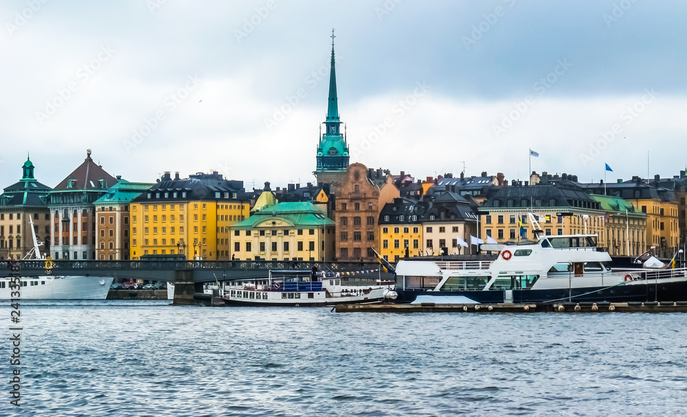 Panoramic view from the boat on waterfront houses in Gamla Stan, tourist boats and Skeppsholmsbron (Skeppsholm Bridge) with Golden Crown in Stockholm Sweden