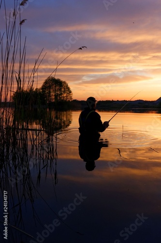 angler standing in a lake and catching the fish during sunset