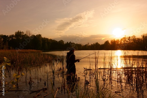 angler standing in a lake and catching the fish during sunset