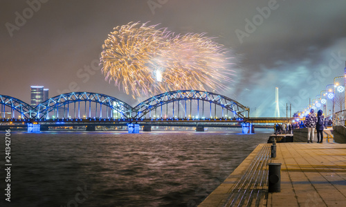 New Year's evening with colorful fireworks in Riga over river Daugava.  Railroad bridge with colorful reflections from fireworks.