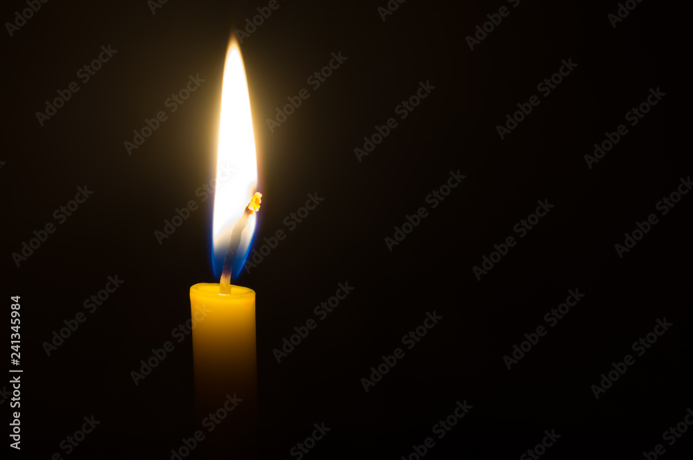 A single candle light glowing on a yellow candle on black background A single candle light glowing on a yellow candle on black background