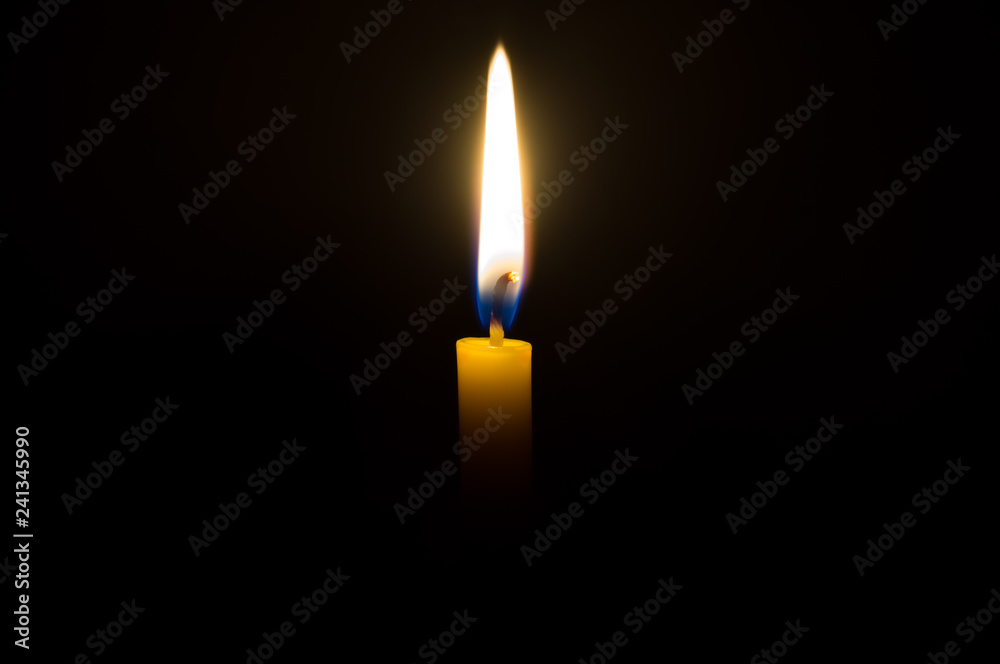 A single candle light glowing on a yellow candle in the middle part of frame on black background A single candle light glowing on a yellow candle in the middle part of frame on black background