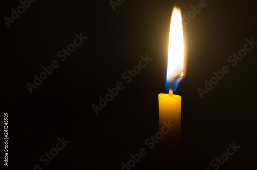 A single candle light glowing on a yellow candle on black background