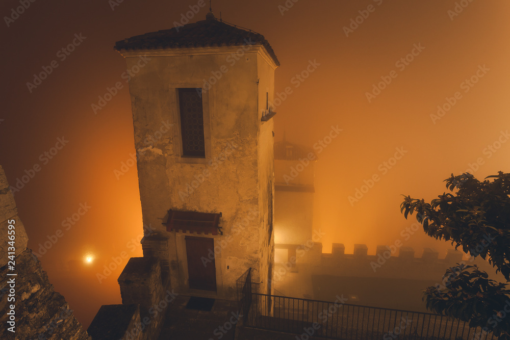 Walls of an ancient castle immersed in the mist during a winter night, Cison di Valmarino, Italy