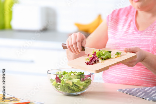 Overweight woman preparing salad in kitchen, space for text. Healthy diet