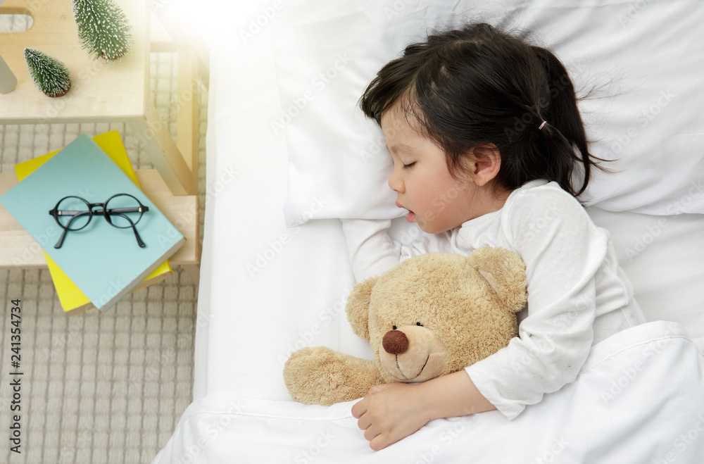 Child girl sleeping with teddy bear on the wooden bed in her bedroom