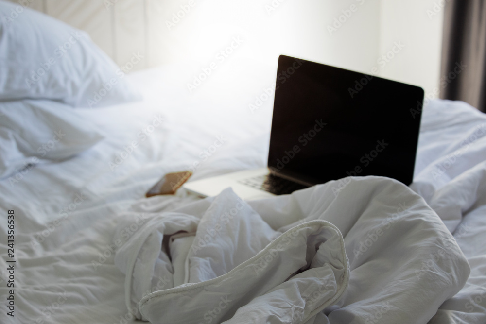 Notebooks and Smartphone placed on the bed with white blankets and pillows in the bedroom. Notebooks and Smartphone placed on the bed with white blankets and pillows in the bedroom.