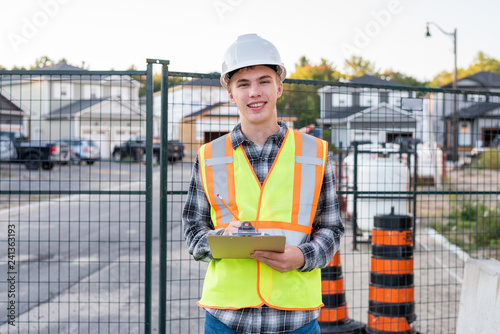 Happy young construction worker wearing safety gear and holding a clipboard.