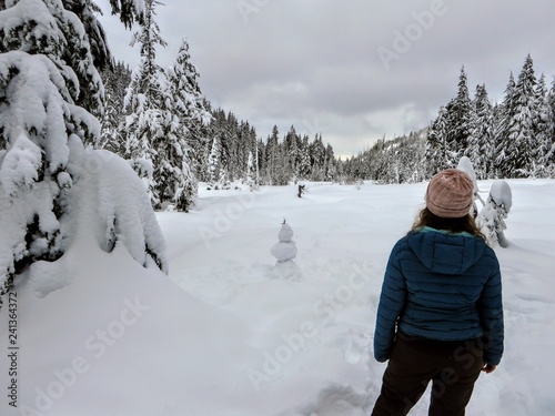 A snowshoer walking and admiring the stunning beauty of the winter landscape on Cypress Mountain as she hikes through groves of Cedar, Hemlock, and Douglas fir trees covered in freshly fallen snow.