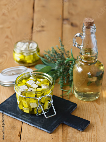 Marinated feta in a glass jar, spices and olive oil on a wooden background