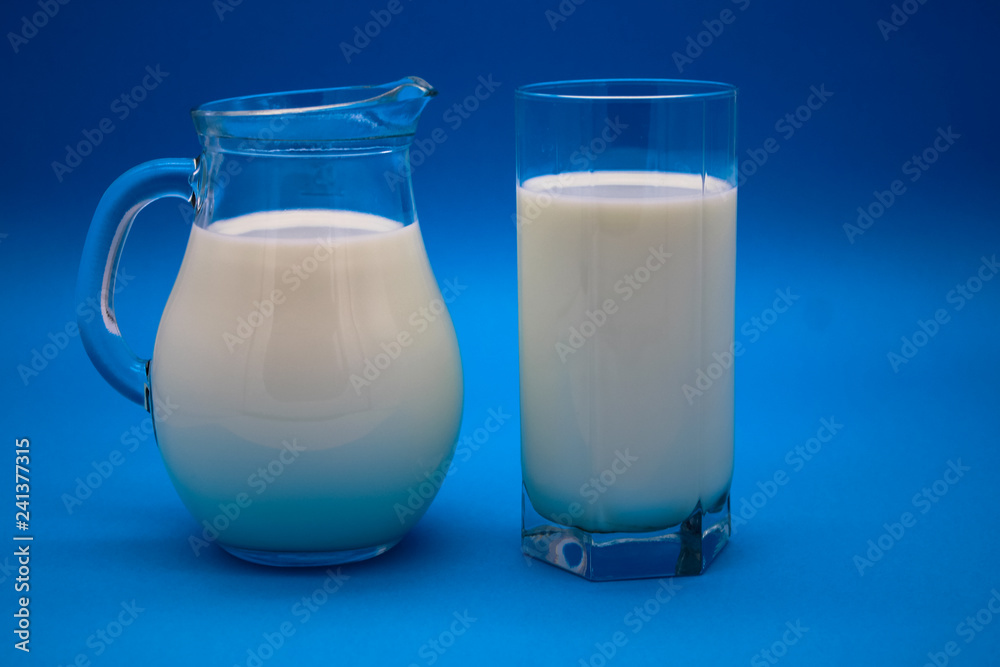 A jug of milk and full glass milk on a blue background
