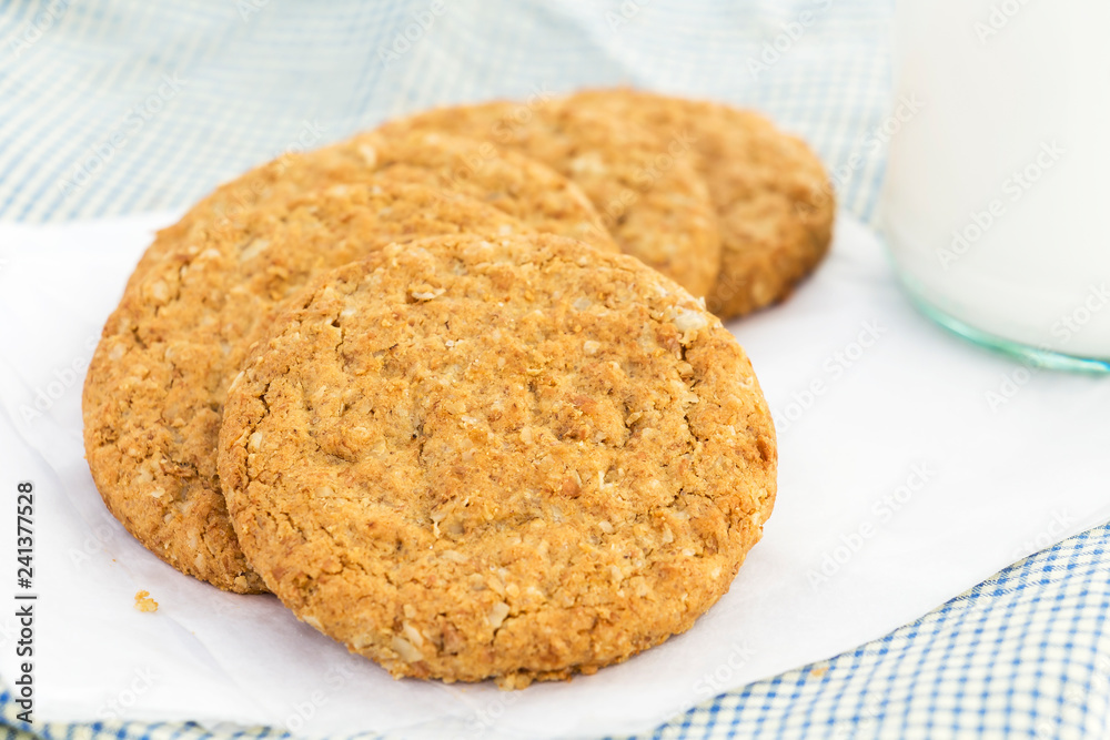 Homemade shortbread cookies made of oatmeal stacked on white paper with glass bottle of milk on blue cloth background. Concept food healthy snack for enjoy in holiday. Homemade shortbread cookies made of oatmeal stacked on white paper with glass bottle of milk on blue cloth background. Concept food healthy snack for enjoy in holiday.