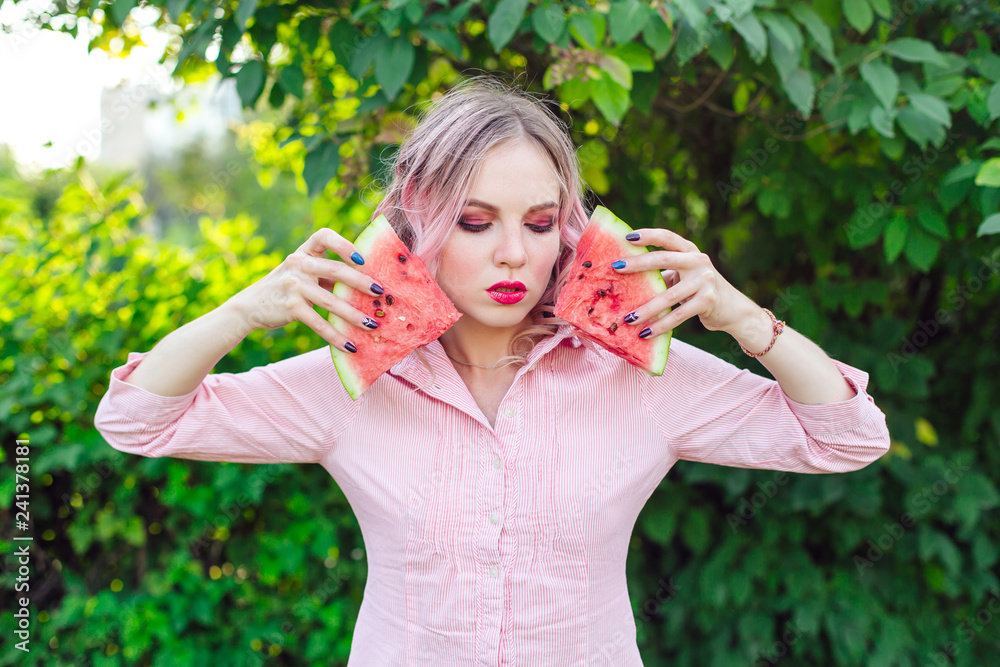 Beautiful young woman with pink hair holding two slices of watermelon in front of her face Beautiful young woman with pink hair holding two slices of watermelon in front of her face
