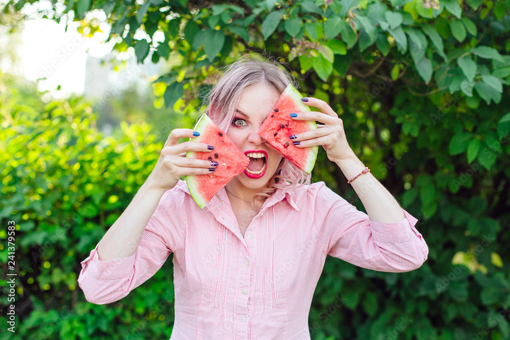 Beautiful young woman with pink hair holding two slices of watermelon in front of her face Beautiful young woman with pink hair holding two slices of watermelon in front of her face