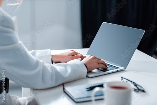 cropped view of woman using laptop with blank screen at office desk at office desk