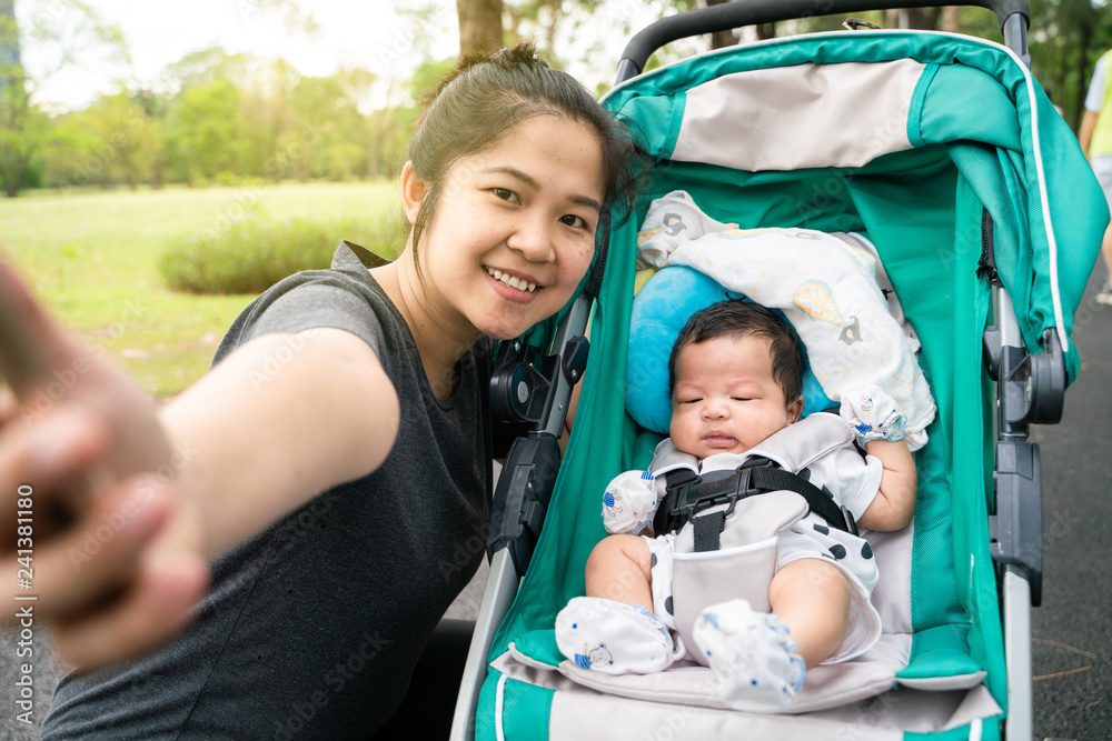 Asian mom with baby boy in stroller walking in green park