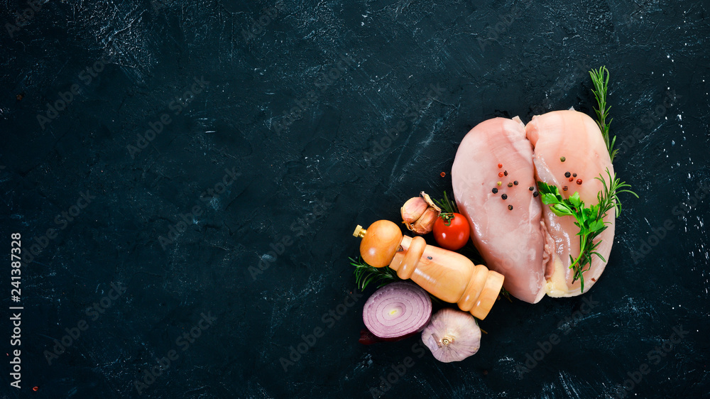 Raw chicken breast with spices and herbs. Barbecue. On a black stone background. Top view. Free copy space. Raw chicken breast with spices and herbs. Barbecue. On a black stone background. Top view. Free copy space.