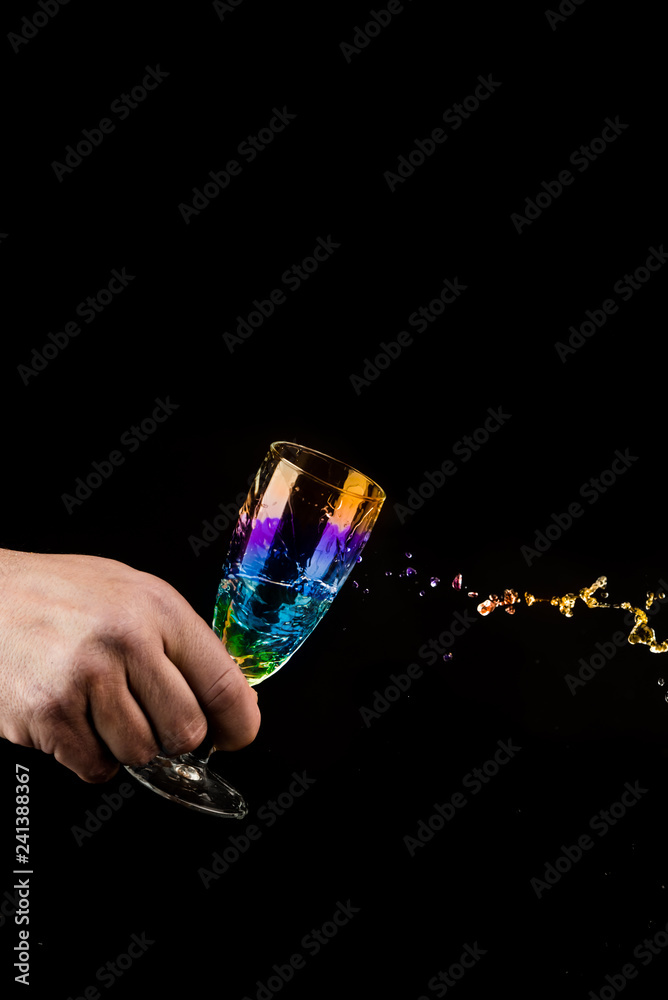 splash of rainbow colors liquid from a glass in the hands on a black background splash of rainbow colors liquid from a glass in the hands on a black background
