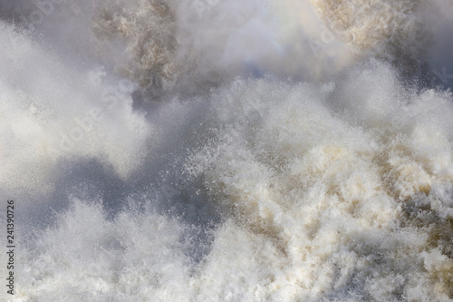 Close up of rough water. On the surface of the water a lot of foam and spray. Abstract background. Empty background. Stormy water. Sea, ocean, waterfall. © Denys