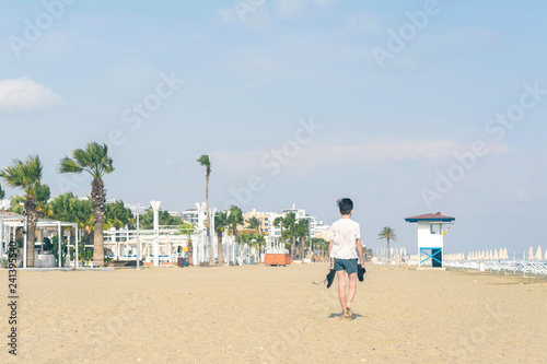 A boy in a T-shirt with sneakers on the sandy Mackenzie beach in Larnaca. Cyprus island