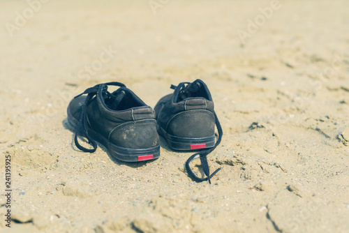 Black sneakers on the sandy beach on the sea background. Summer and travel concept