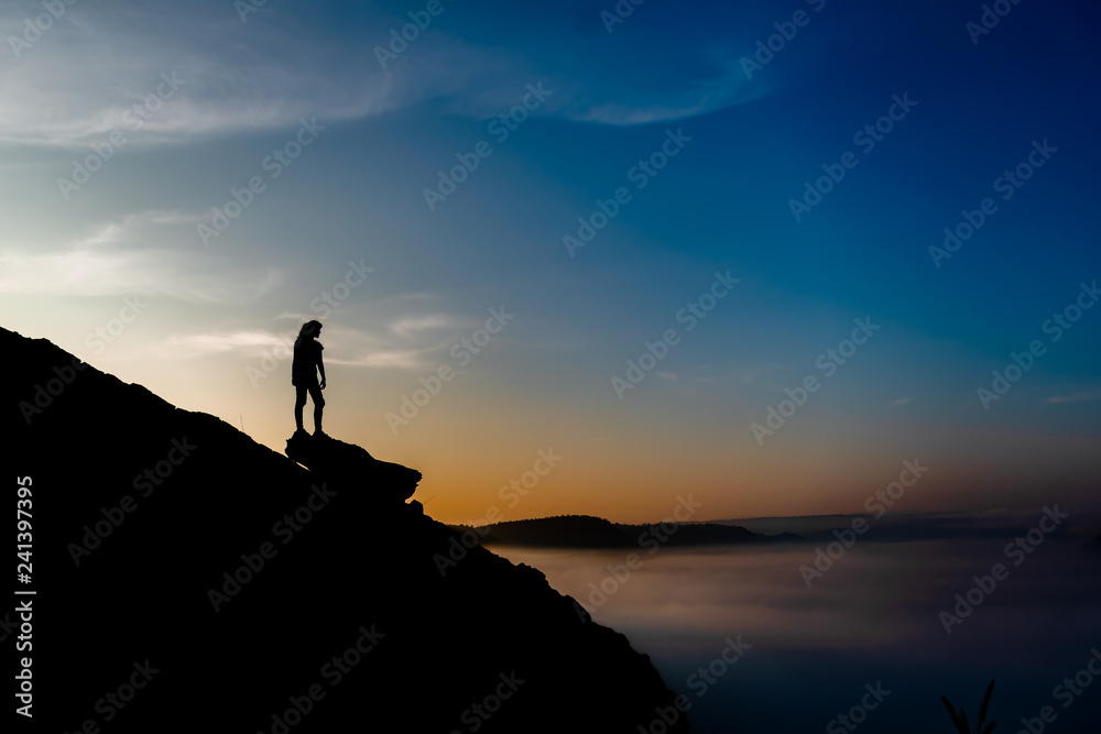 Woman stands alone on the rock of mountain.Colorful mist in valley silhouette scene.