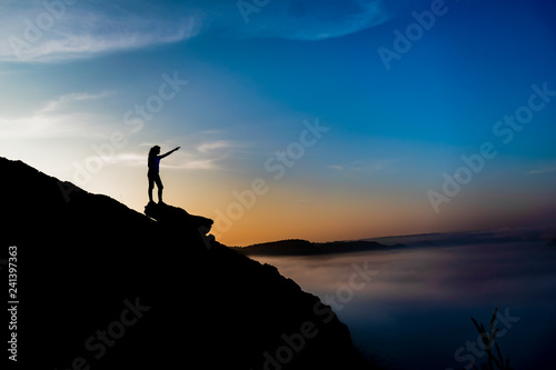 Woman stands alone on the rock of mountain.Colorful mist in valley silhouette scene.
