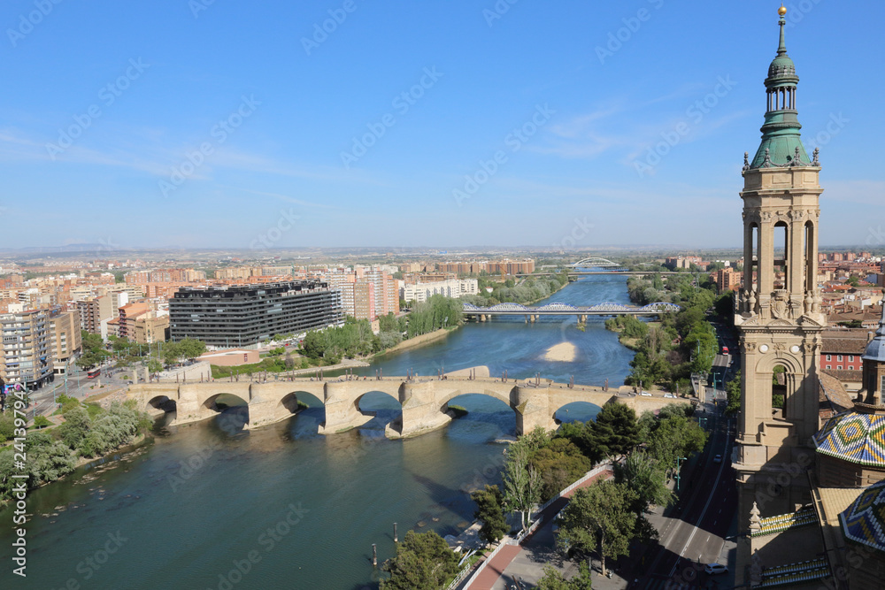 A landscape of Zaragoza with the Puente de Piedra and Puente de Hierro bridges, the Ebro river and a Pilar Cathedral bell tower, in Aragon, Spain