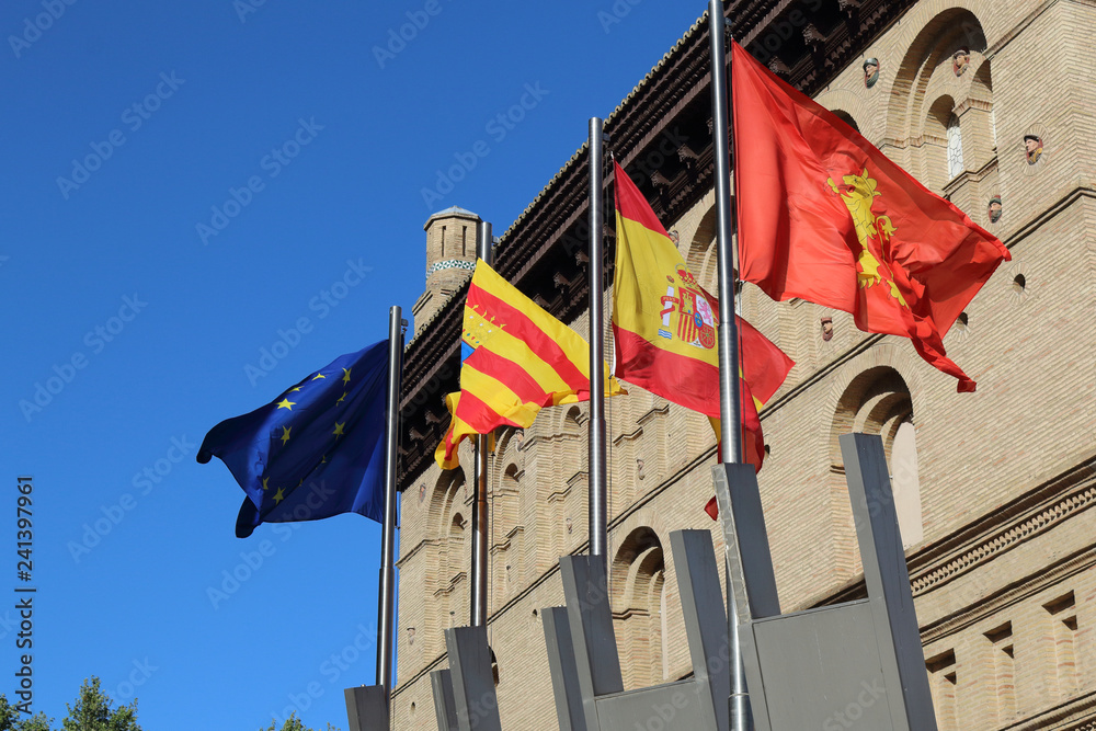 The Zaragoza, Aragonese, Spanish and European flags flapping against a blue sky om font of the city hall during a sunny summer day in Zaragoza, Spain