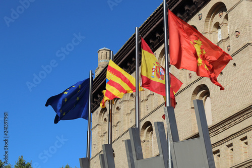 The Zaragoza, Aragonese, Spanish and European flags flapping against a blue sky om font of the city hall during a sunny summer day in Zaragoza, Spain